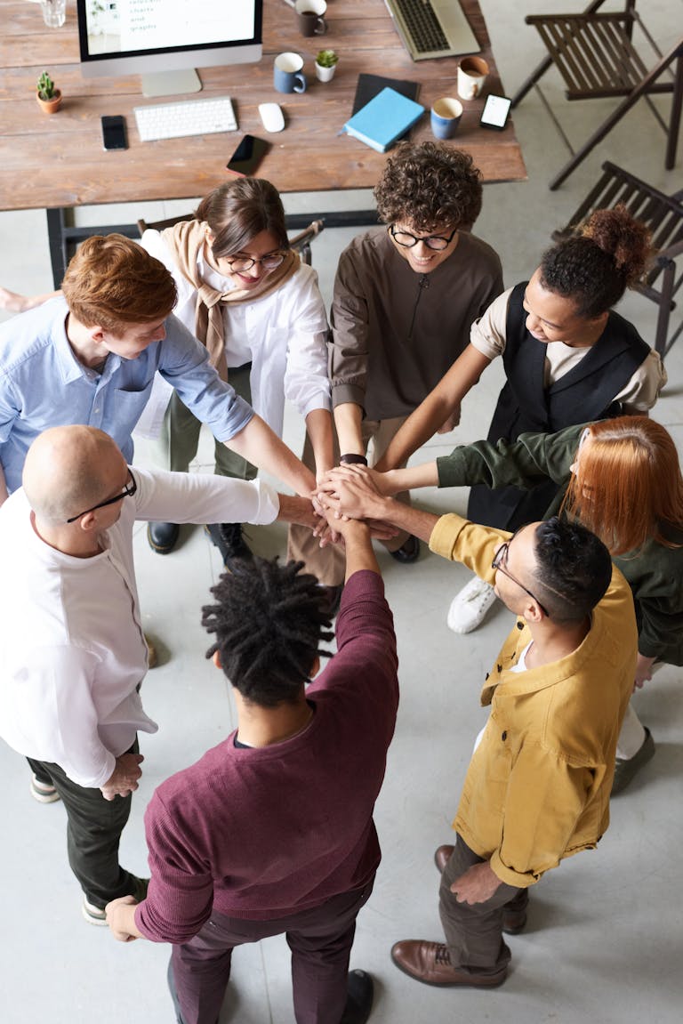 Kuva A diverse group of professionals joins hands in a team-building exercise indoors.